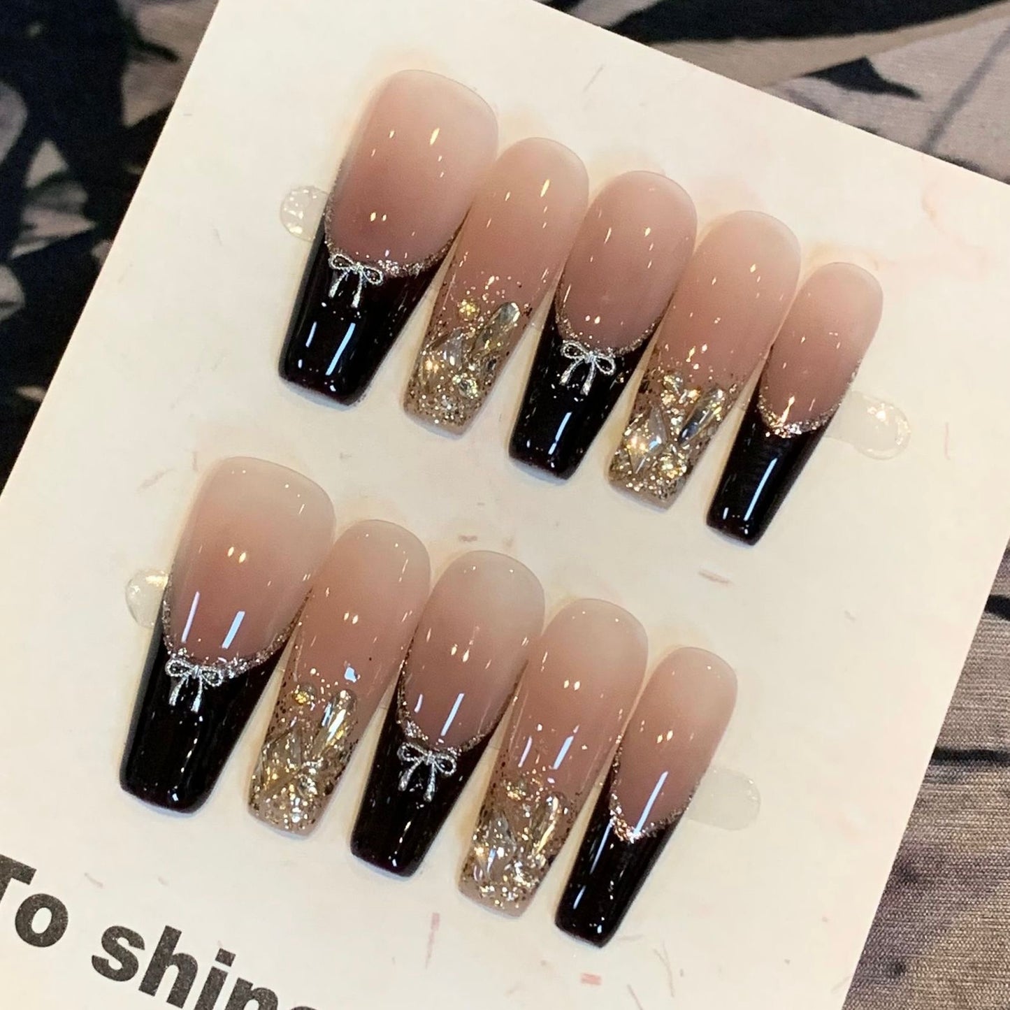 Product Features:

Theme: Glimmering Noir Bow
Shape: Long Square
Design: Gradient sheer brown with black and sparkling gold French tips
Embellishments: Charming bows
Style: Minimalist and luxurious, perfect for autumn
Quality: High-quality, handmade craftsmanship